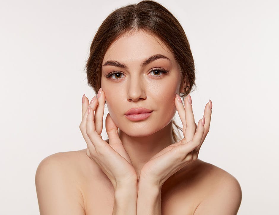 woman with hair up with both hands touching both cheekbones