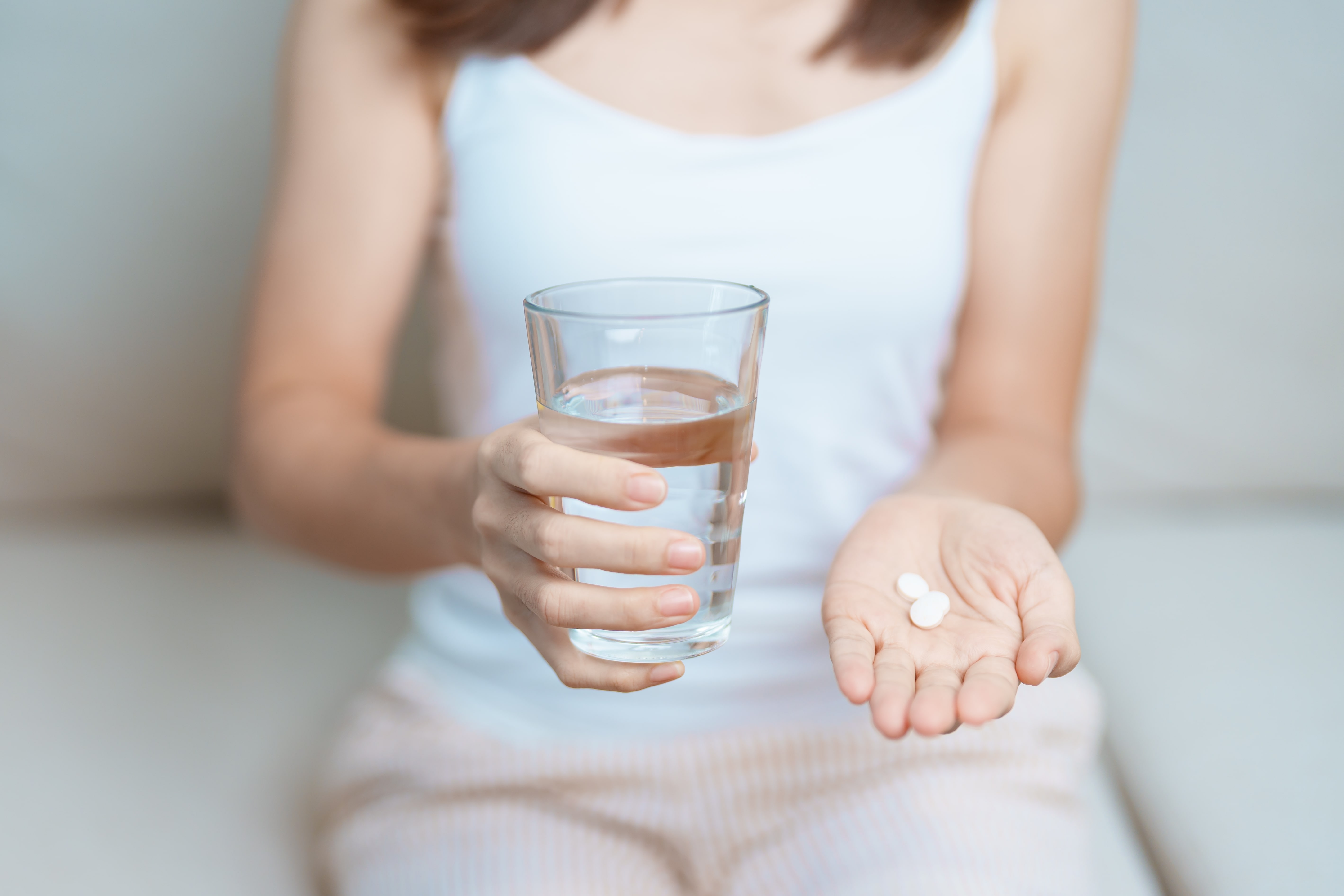 A person holding a glass of water and an antibiotic in their hand
