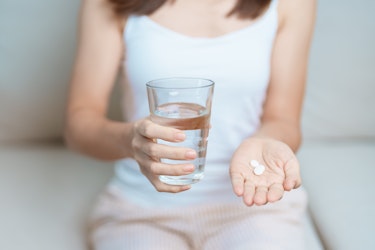 A person holding a glass of water and an antibiotic in their hand