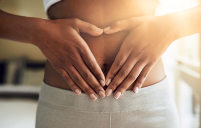 A lady touching her gut to form a heart shape in her hands
