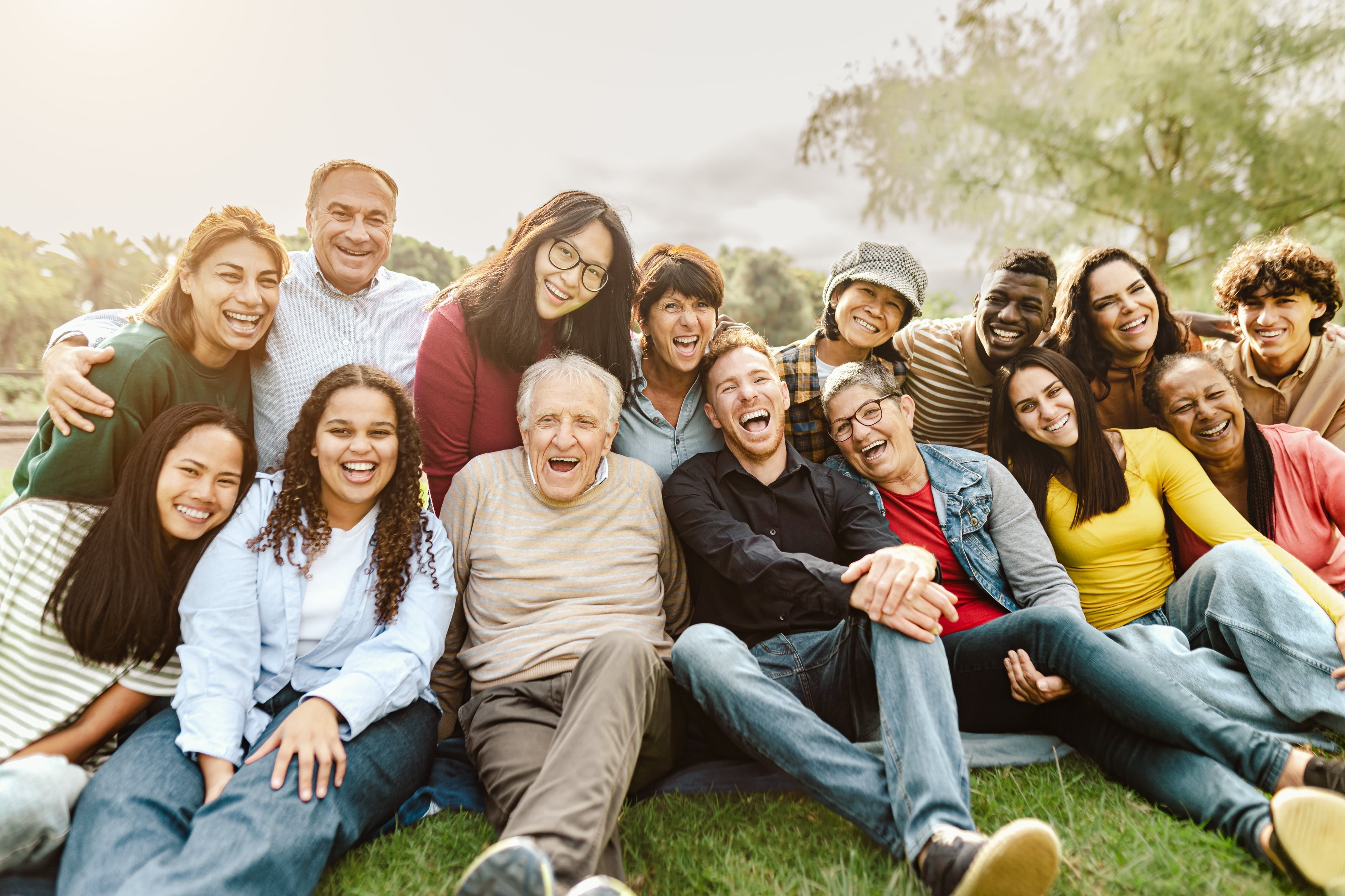 A group of people of various ages sat together in a park setting and happily laughing together