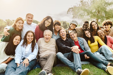 A group of people of various ages sat together in a park setting and happily laughing together