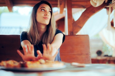 A lady refusing to eat food that is on a plate in front of her