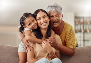 3 generations of females on a sofa together smiling and hugging each other