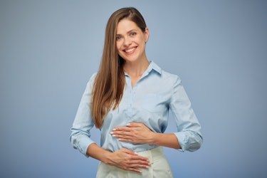 A lady smiling whilst holding her stomach to indicate that she has a happy gut