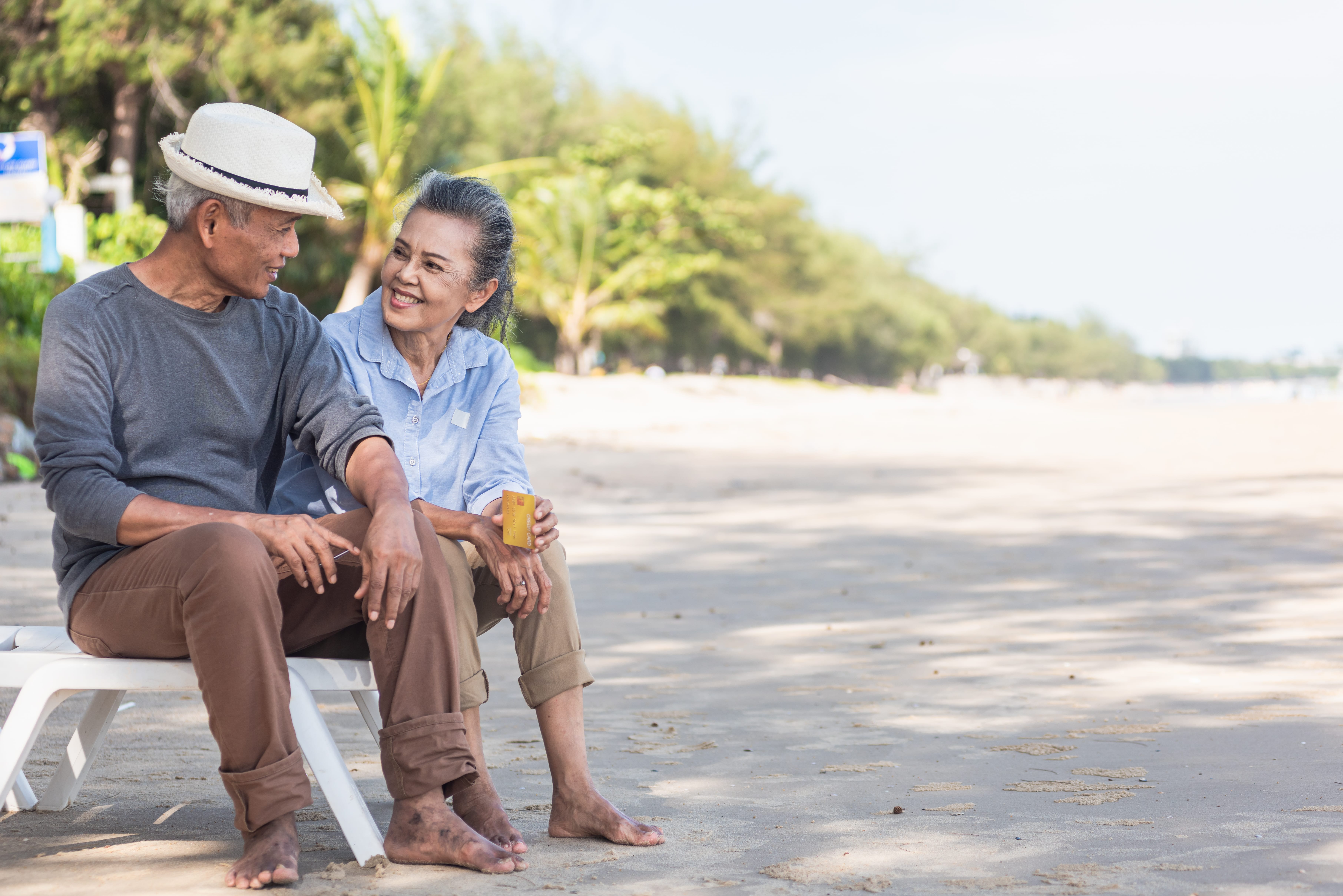 An older couple sat on the beach happily staring into each others eyes