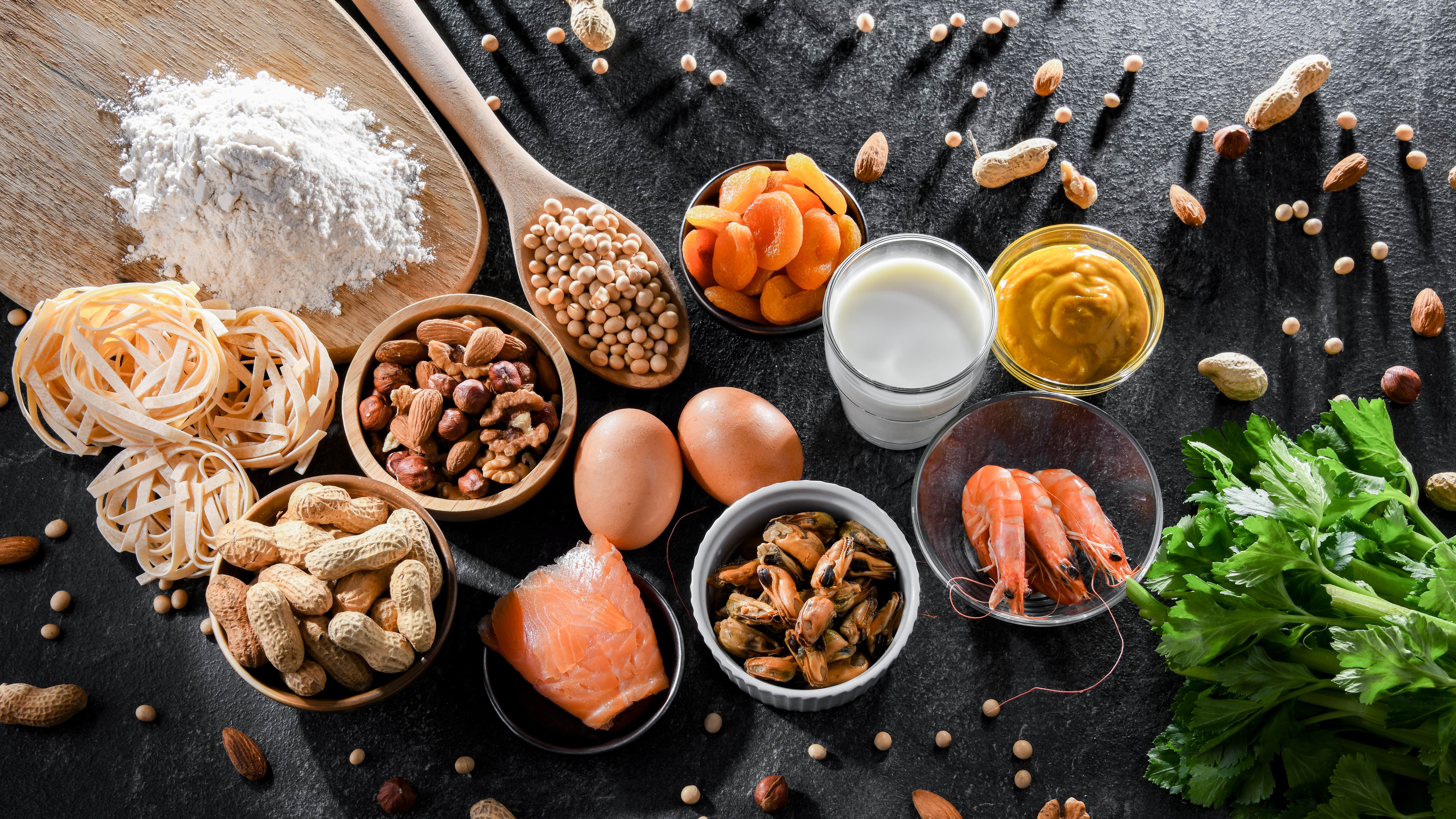 Common food allergens including nuts, milk, eggs, shellfish, wheat, soy and leafy greens displayed on a dark surface, highlighting ingredients linked to food allergies and intolerances