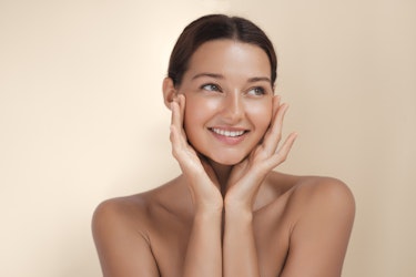 Smiling woman with clear, healthy skin touching her face, promoting natural skincare and glowing complexion