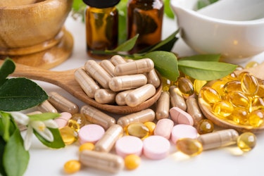 Assorted herbal supplements, vitamins and capsules on wooden spoons with natural leaves and glass bottles in the background
