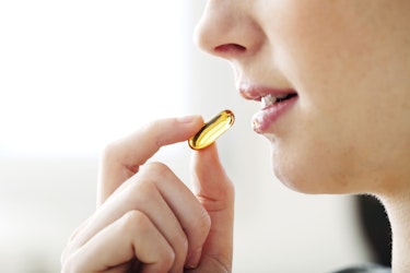 Close-up of person about to take a softgel supplement capsule, held near lips