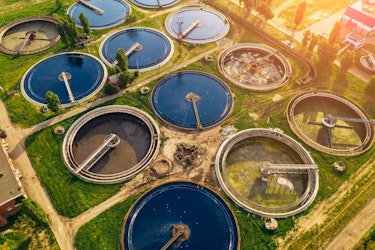 Aerial view of a wastewater treatment plant with circular sedimentation tanks surrounded by greenery