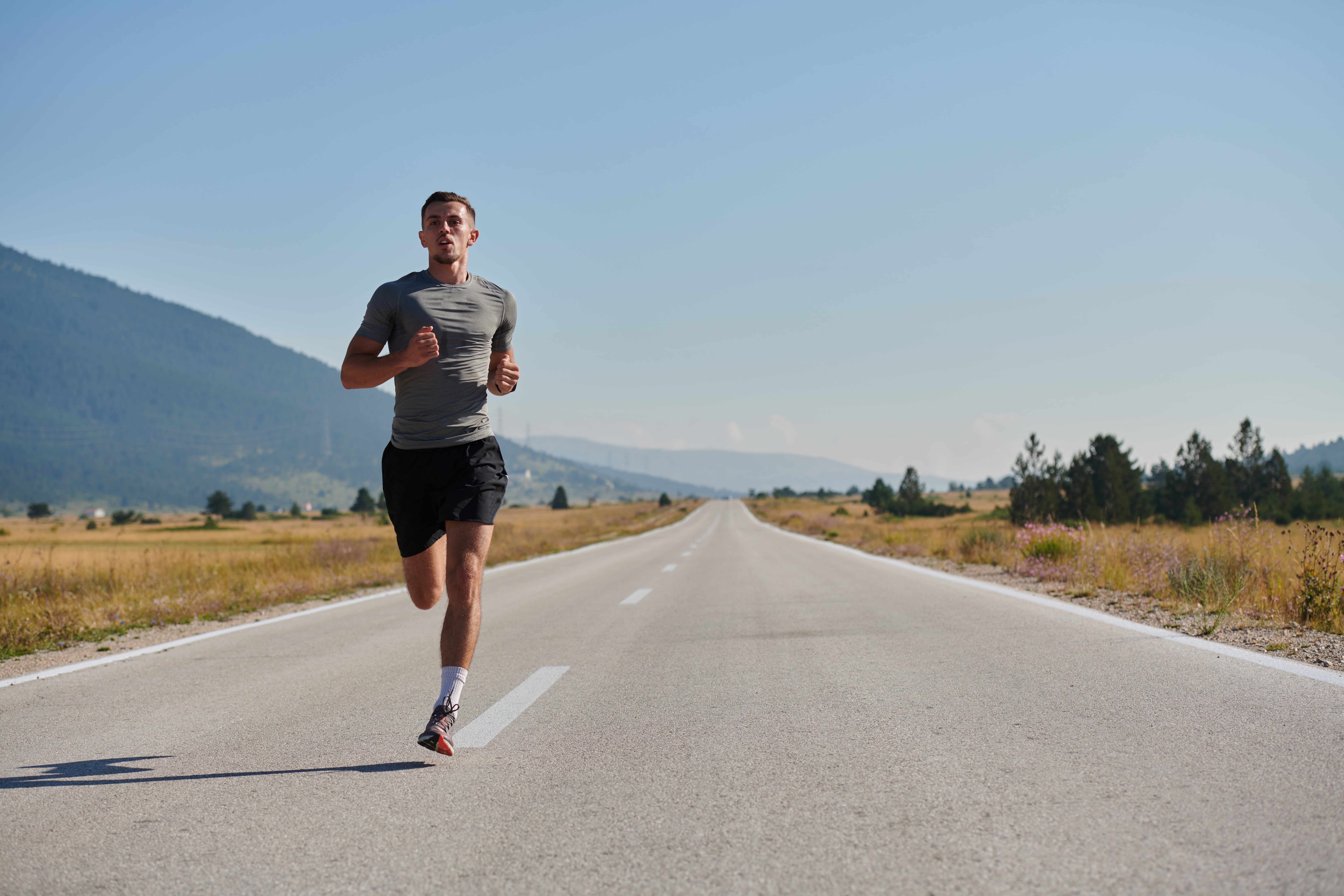 Man running alone on an open rural road with mountains in the background, representing fitness, endurance and outdoor exercise.