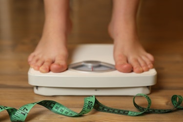 Person standing on a bathroom scale with a green measuring tape on the floor, symbolising healthy weight management and progress with GLP-1 treatment and NAD+ support.
