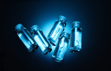 Five clear medical vials containing liquid solution under blue light, representing NAD+ injections or supplements used in research on energy, ageing and cellular health.