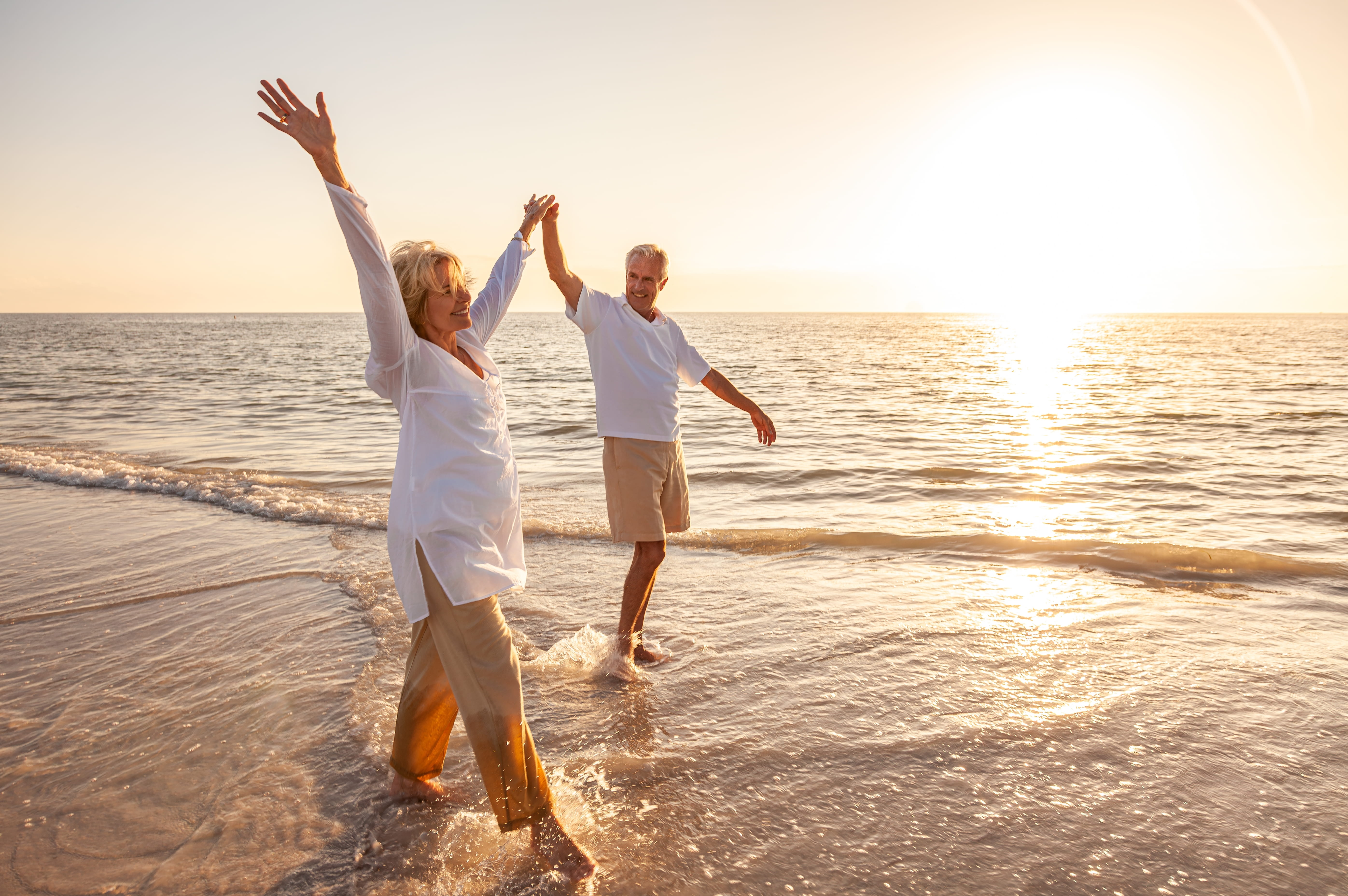 A joyful senior couple walking playfully on a beach at sunset with their arms raised, visually representing the vitality, healthy ageing, and sustained energy levels associated with the cellular synergy of Spermidine and NAD+