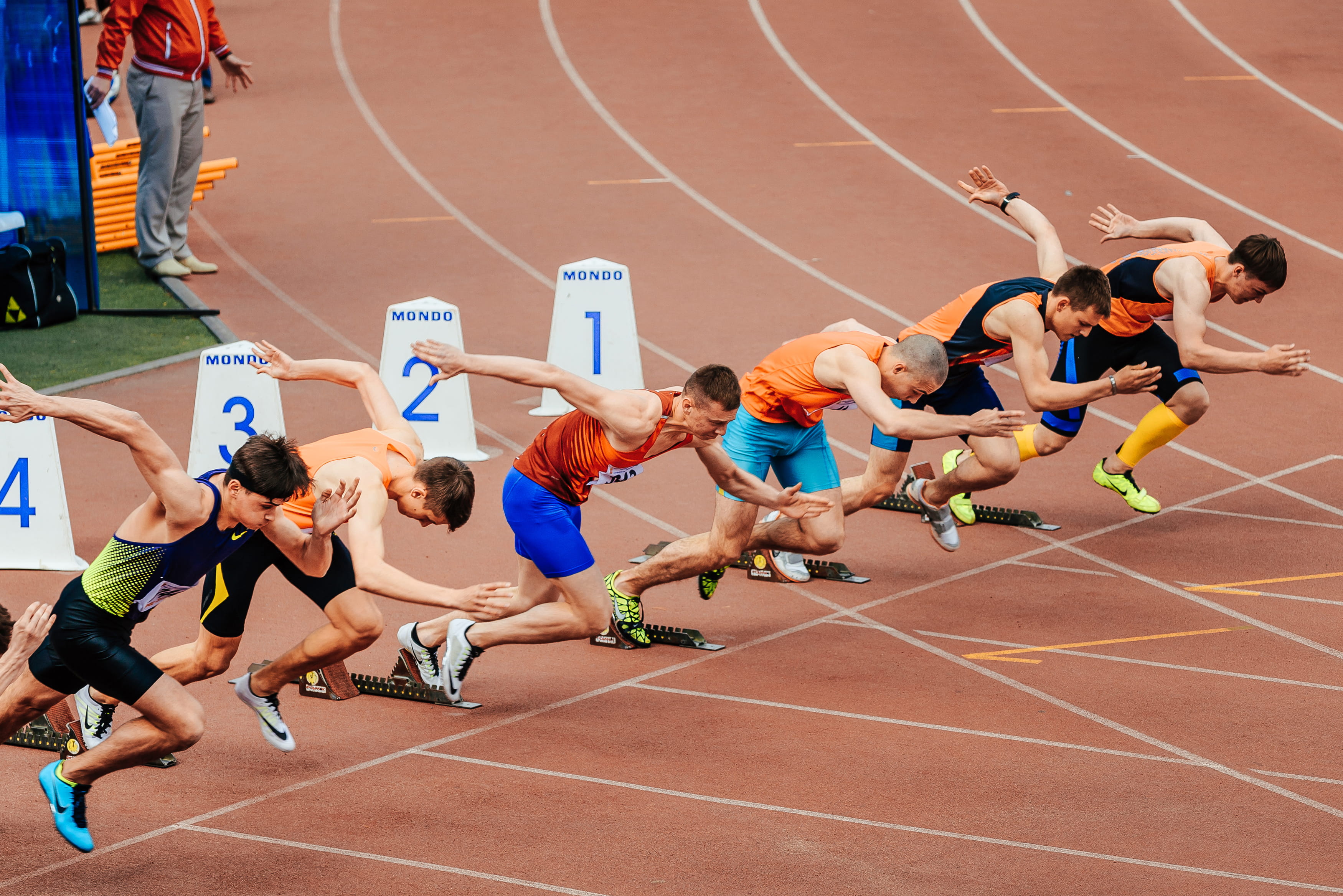 Group of sprinters exploding out of the starting blocks on an athletics track during a race