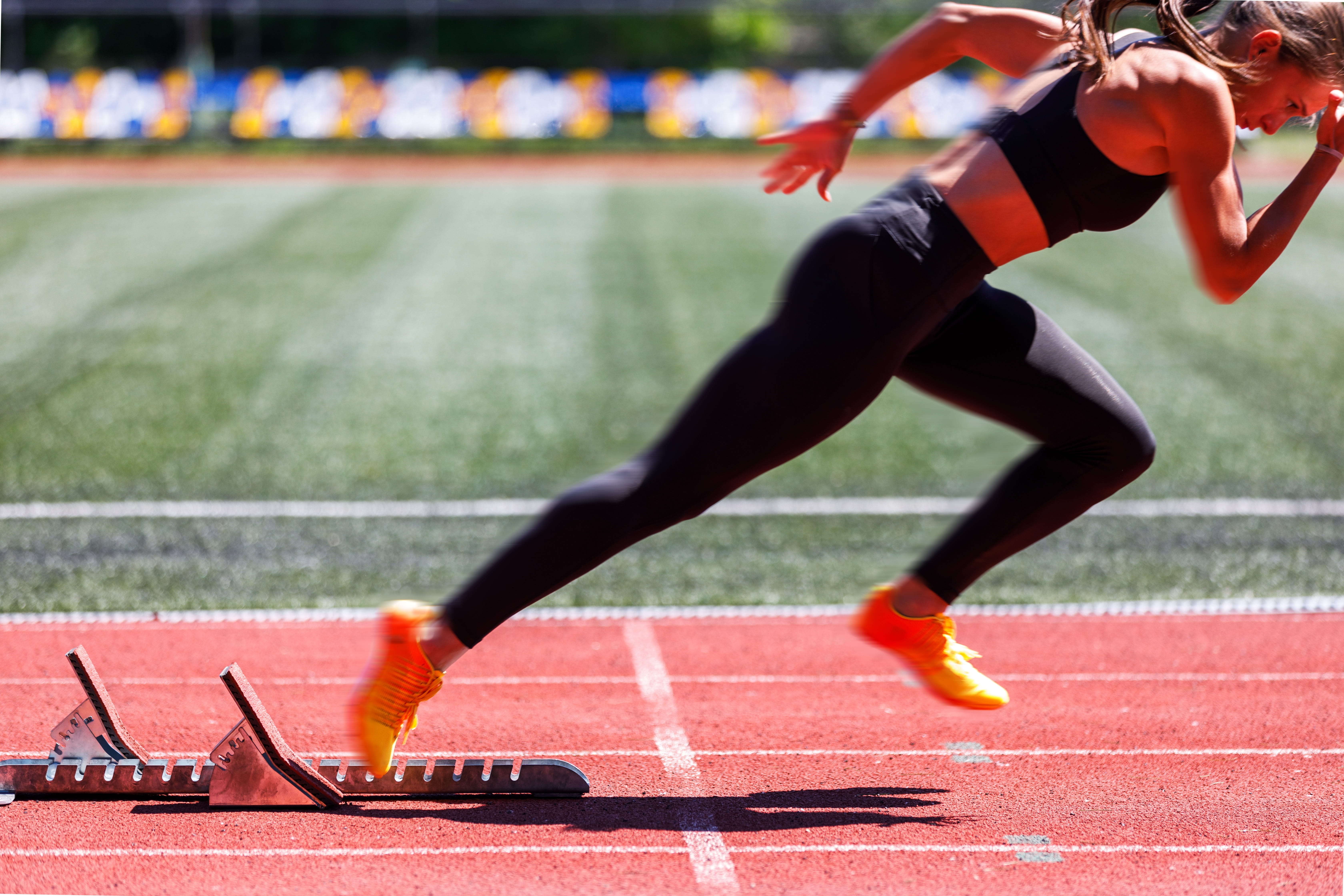 Sprinter in orange spikes driving out of the starting blocks on a sunny athletics track