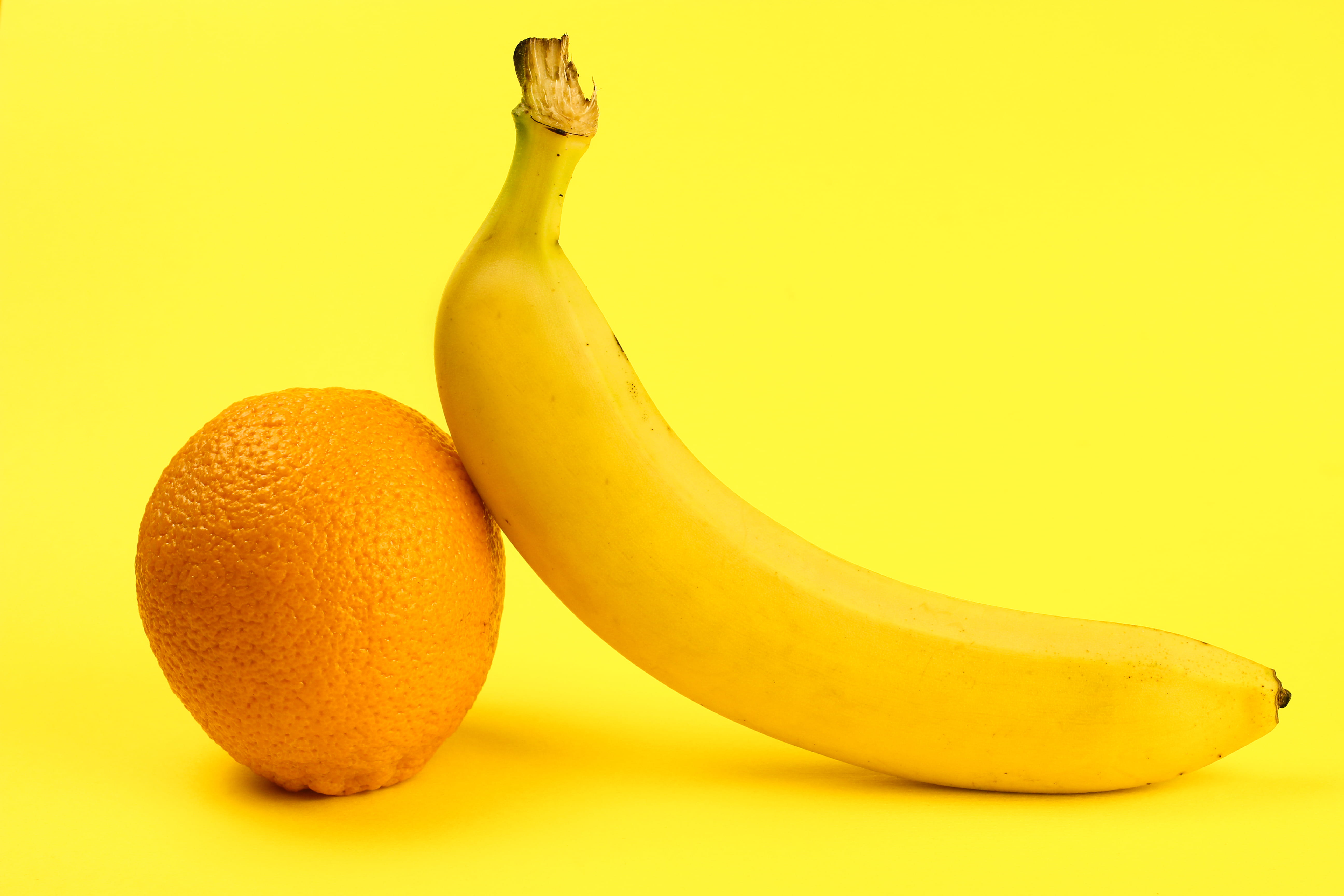 An orange and a banana side by side against a bright yellow background