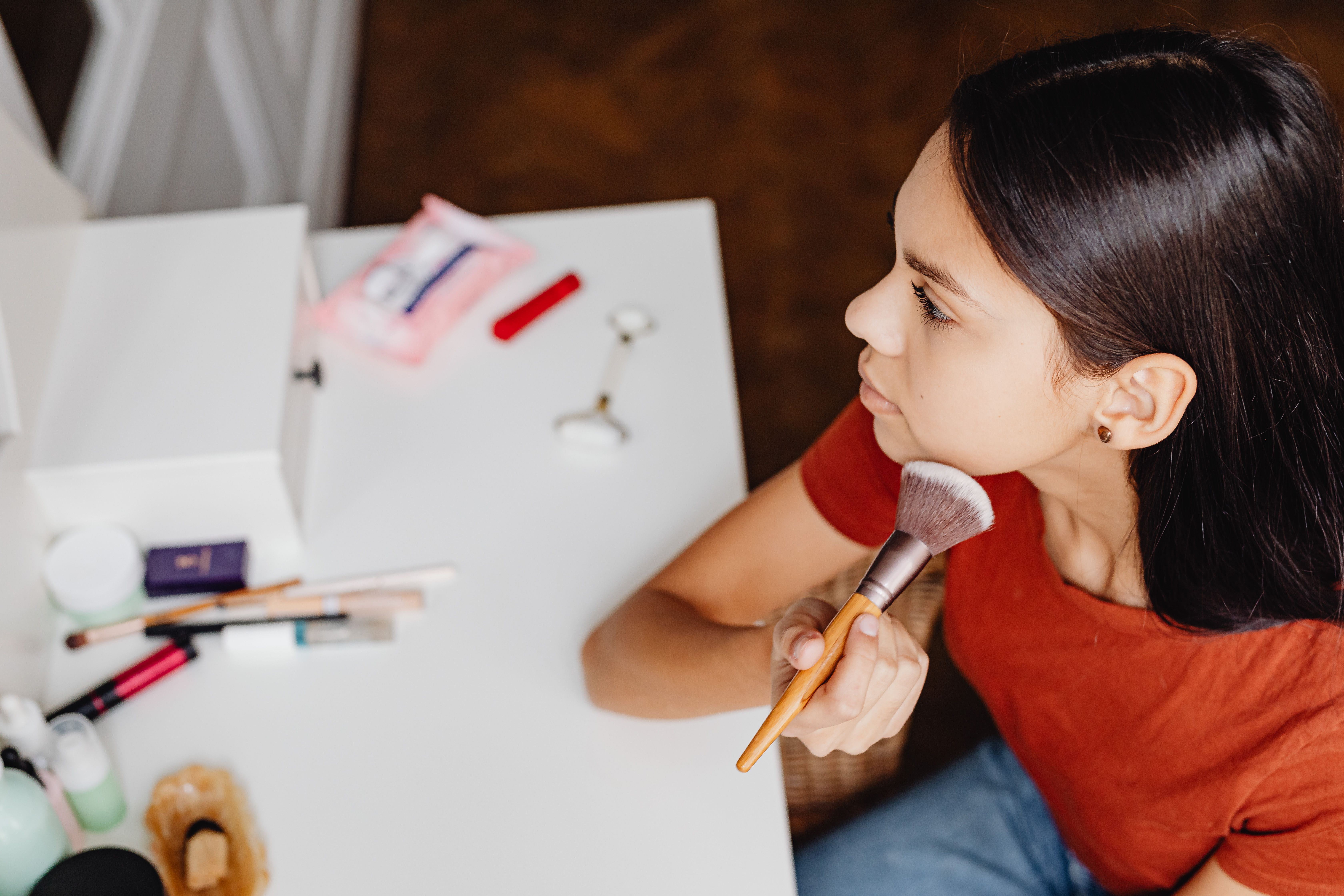 Young person applying makeup with a brush at a white table, cosmetic products laid out beside them