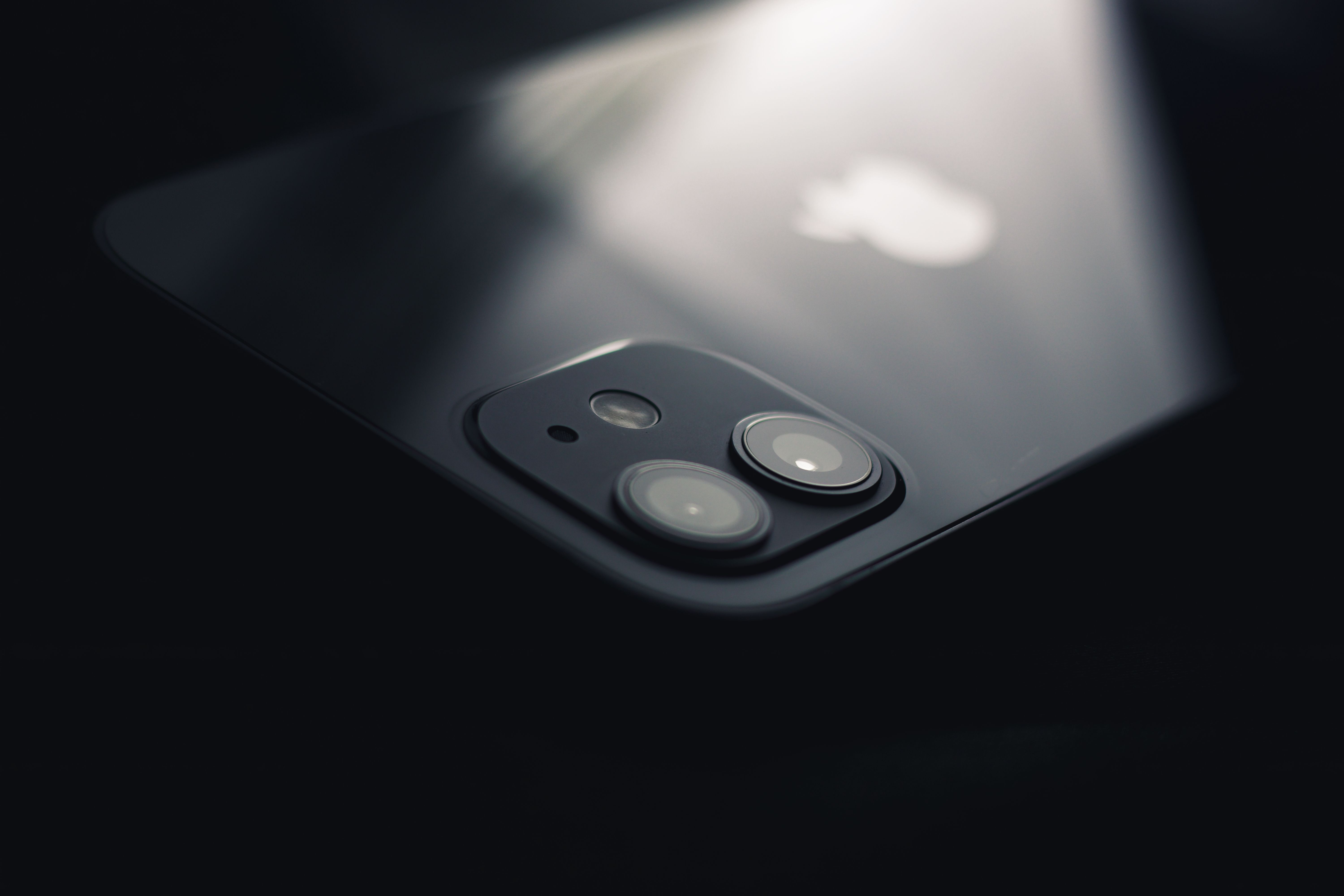 Dark, moody close-up of an iPhone's rear camera, an Apple device shown against a black backdrop