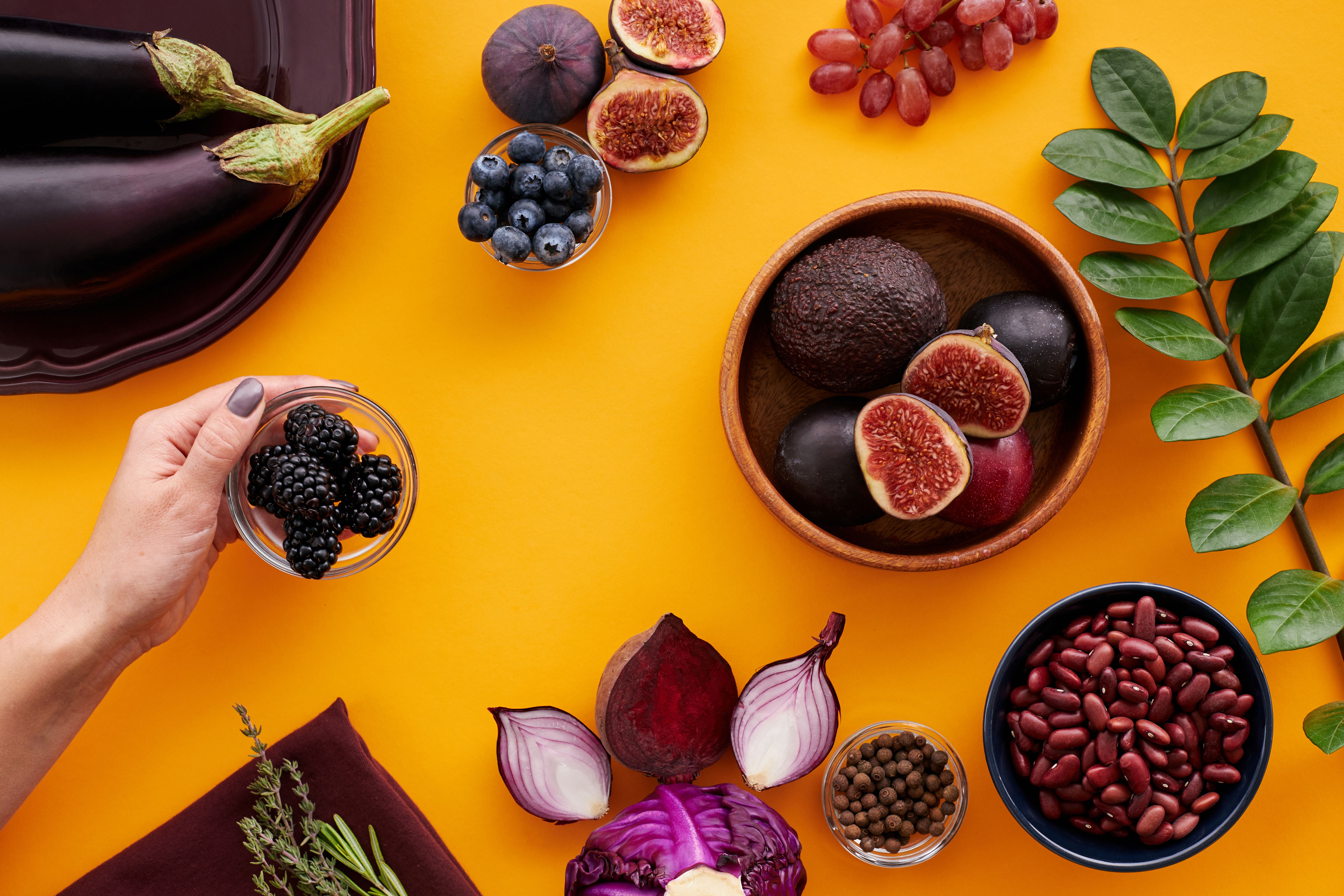 Overhead spread of purple foods including aubergine, figs, blueberries, blackberries, red onion and beans