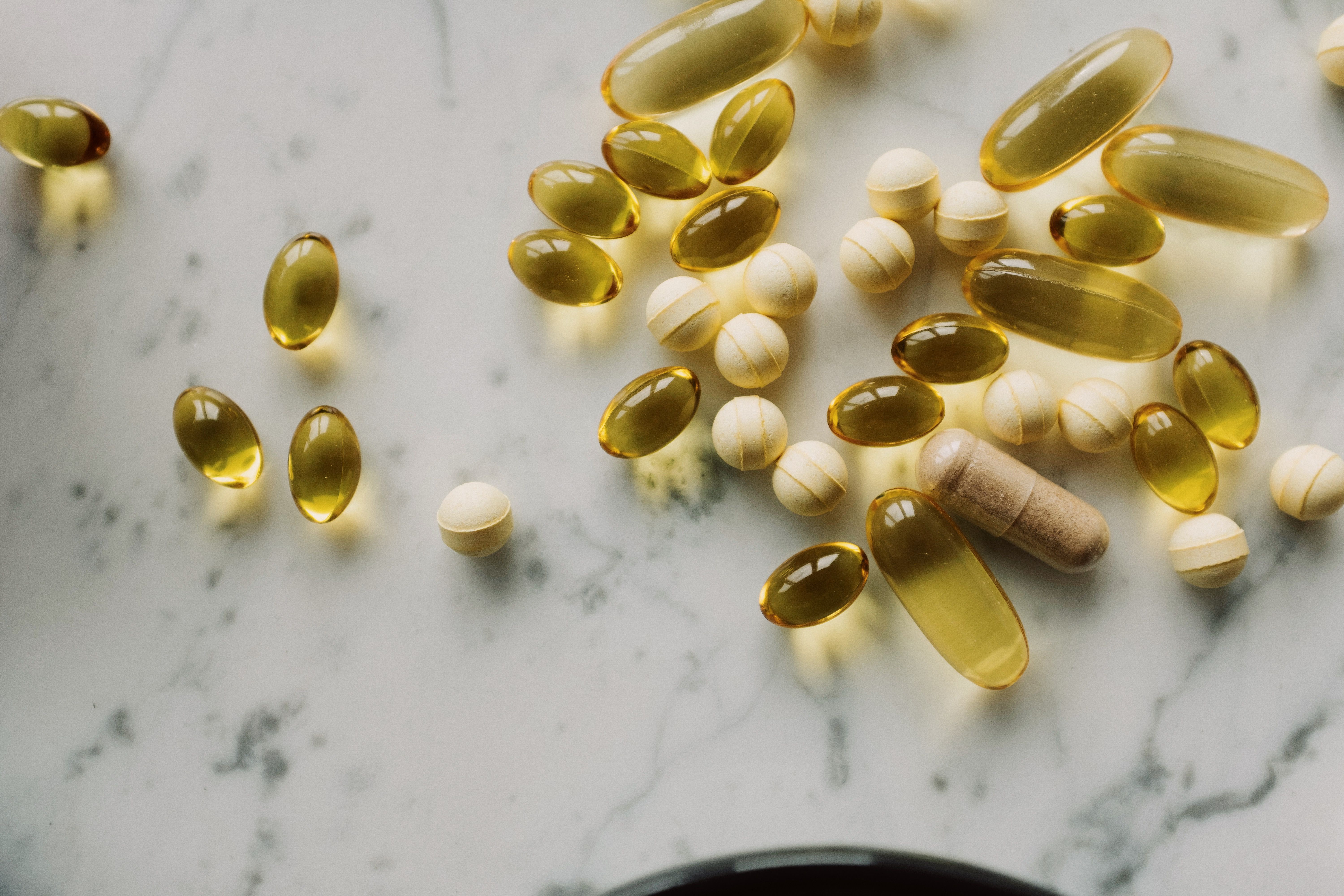 Assorted supplement capsules and softgels scattered on a white marble surface