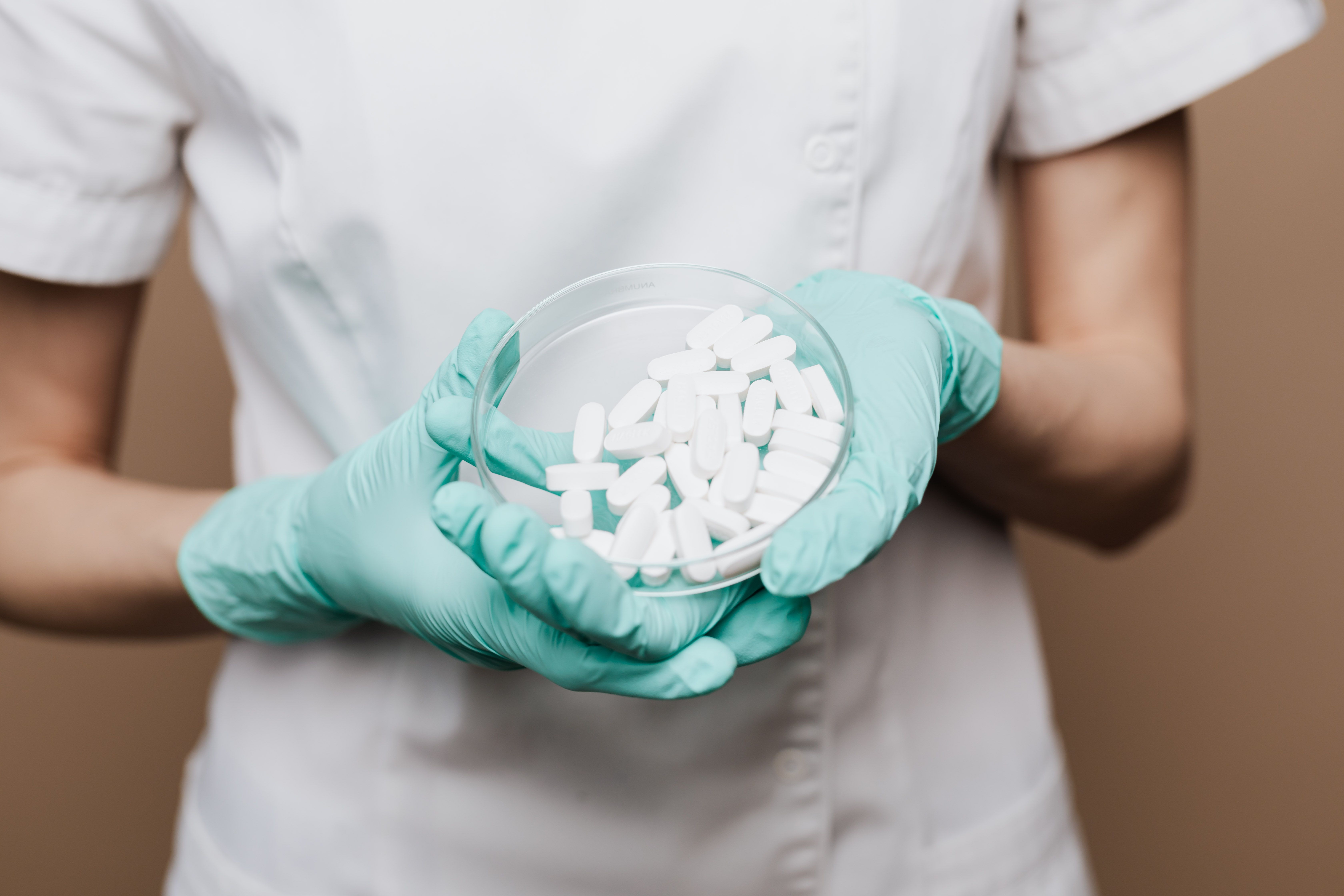 Healthcare worker in green gloves holding a dish of white tablets or capsules