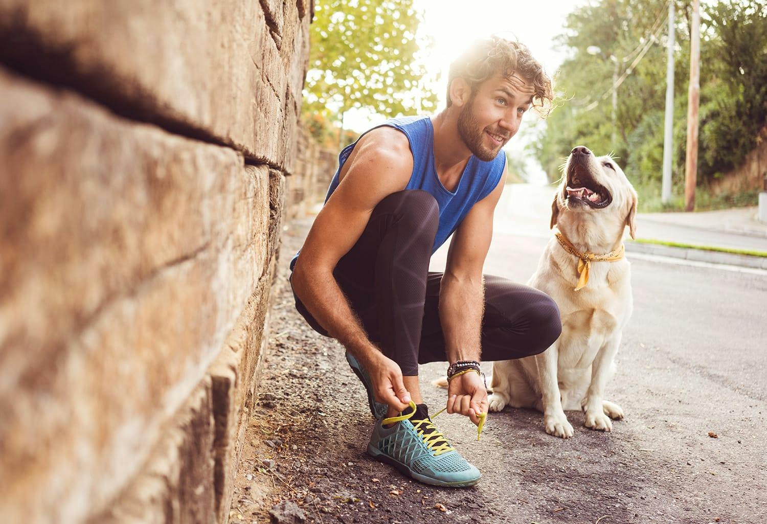 Man bending down to tie his shoe next to his dog