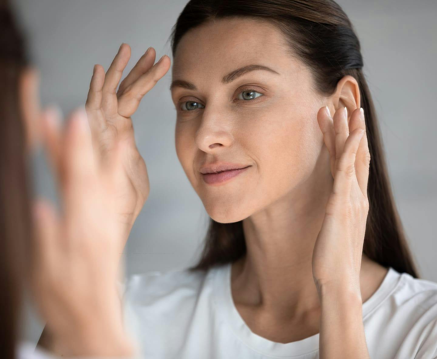 woman looking in mirror touching her face