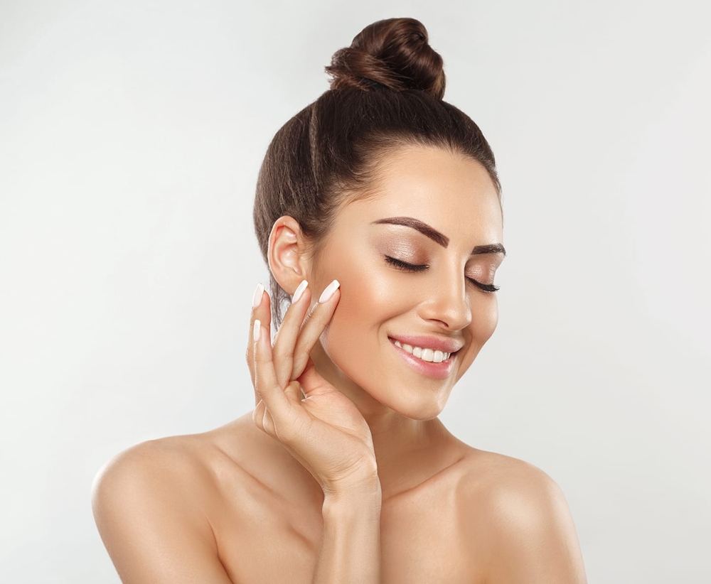 woman with hair tied up smiling and touching her cheek
