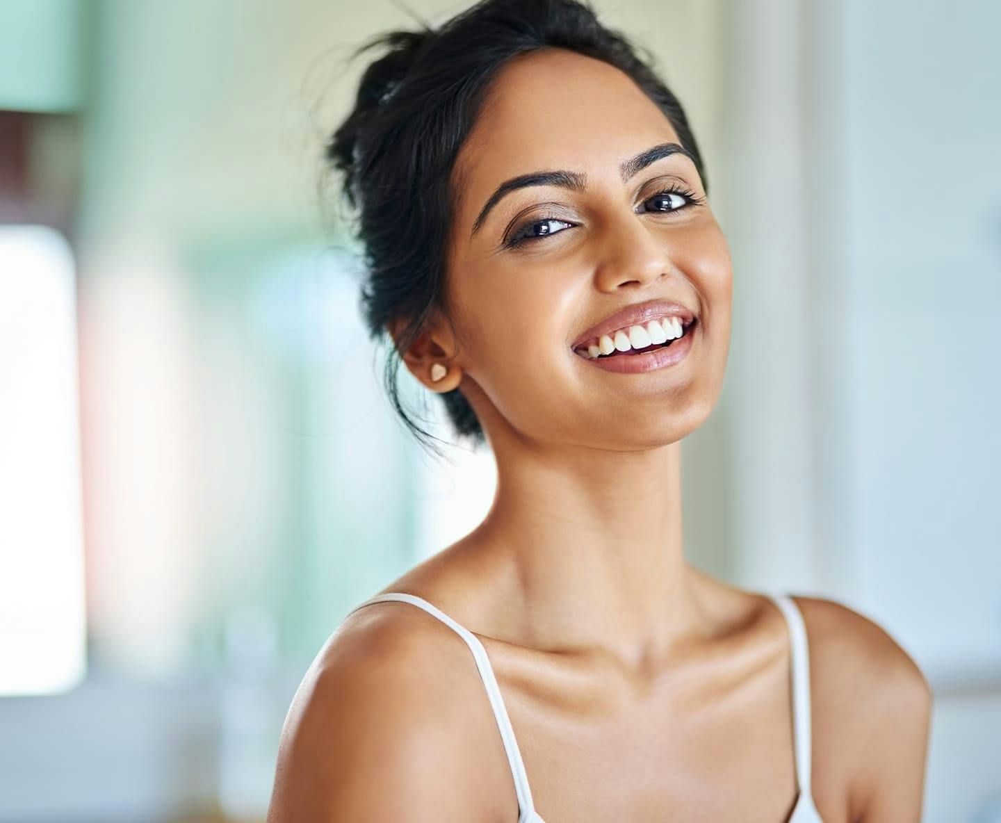 woman in white tanktop and hair tied up smiling forward