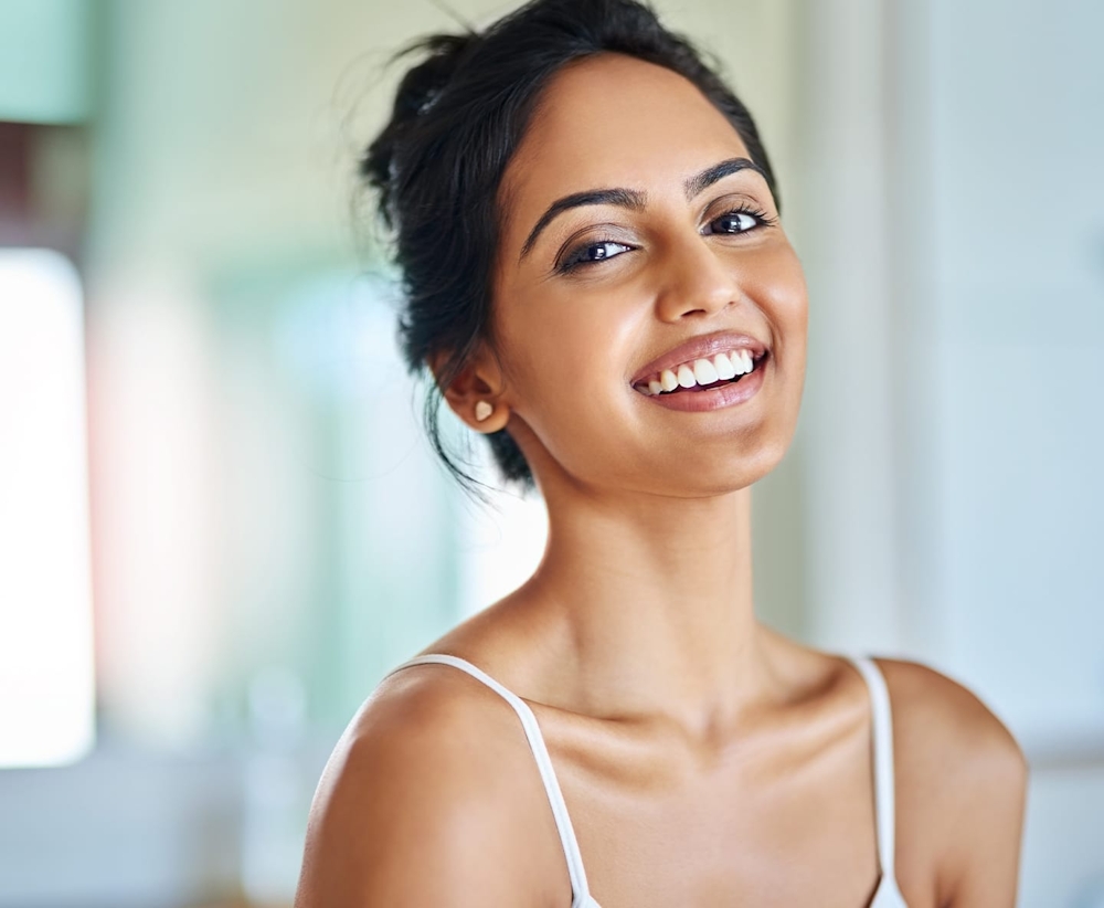 woman in white tanktop and hair tied up smiling forward