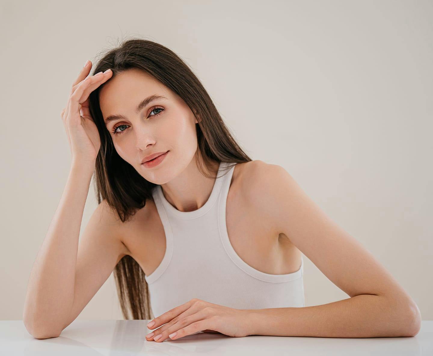 woman with long straight hair leaning on table with hand on her forehead