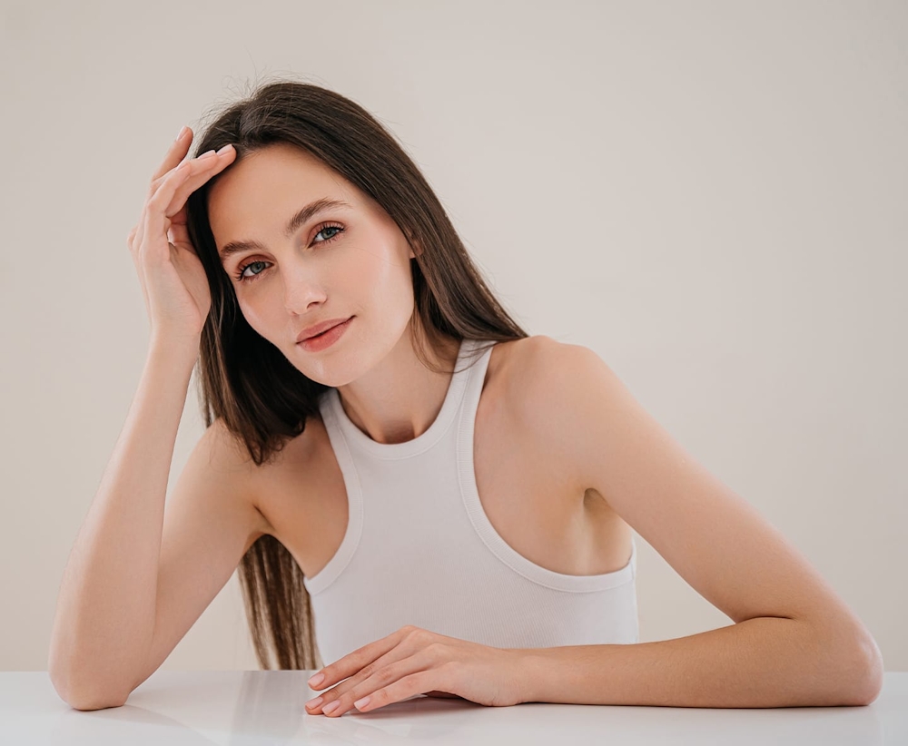 woman with long straight hair leaning on table with hand on her forehead