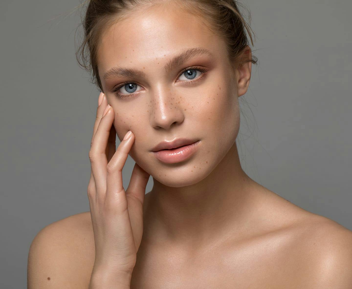 woman with hair up touching her face with hand
