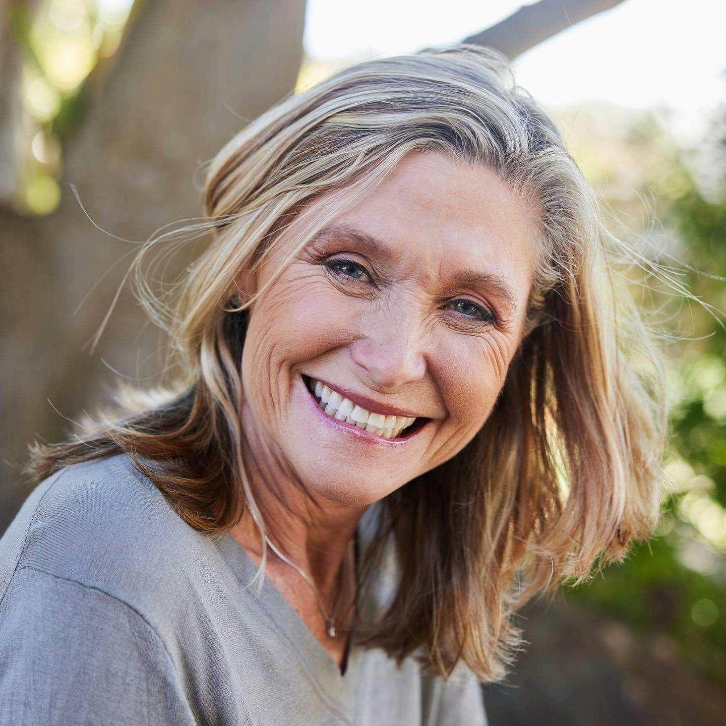 older woman smiling with tree in the background