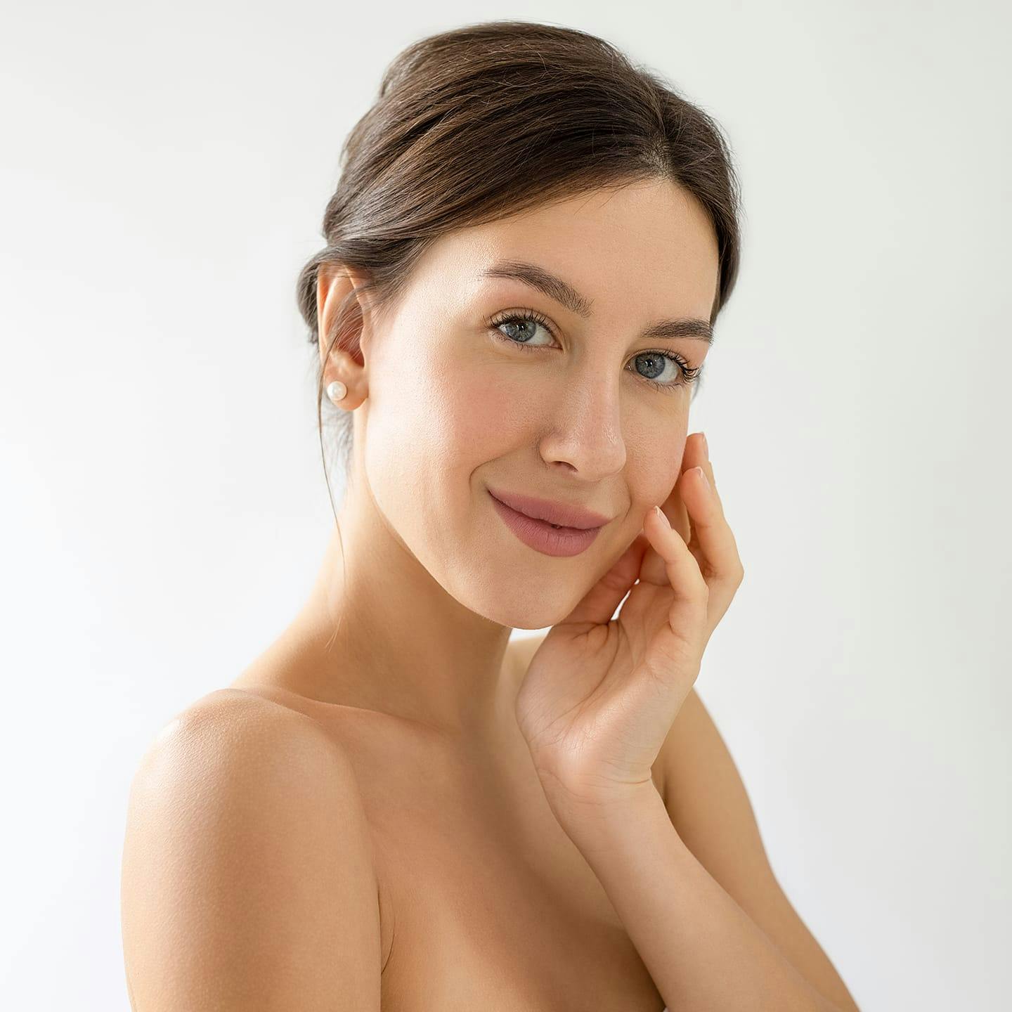 woman wiht hair tied back smiling with hand on her cheek