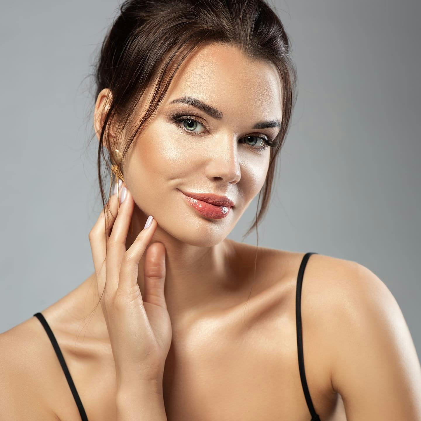 woman with hair tied up touching the back of her jaw