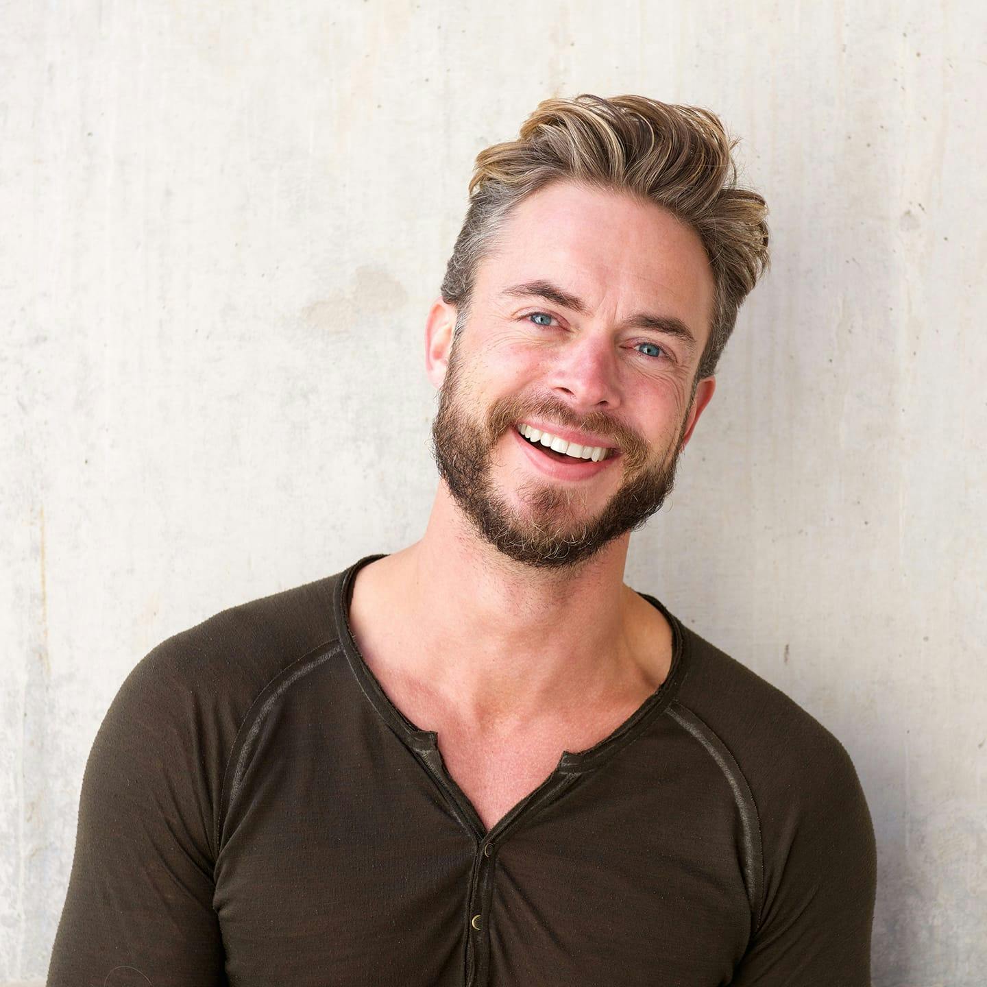 man smiling with brown shirt slightly leaning his head