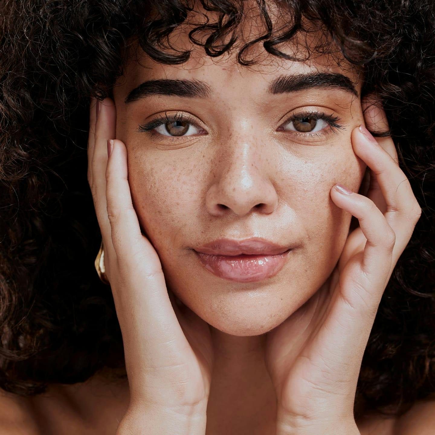 close up of woman with curly hair touching her face with her hands