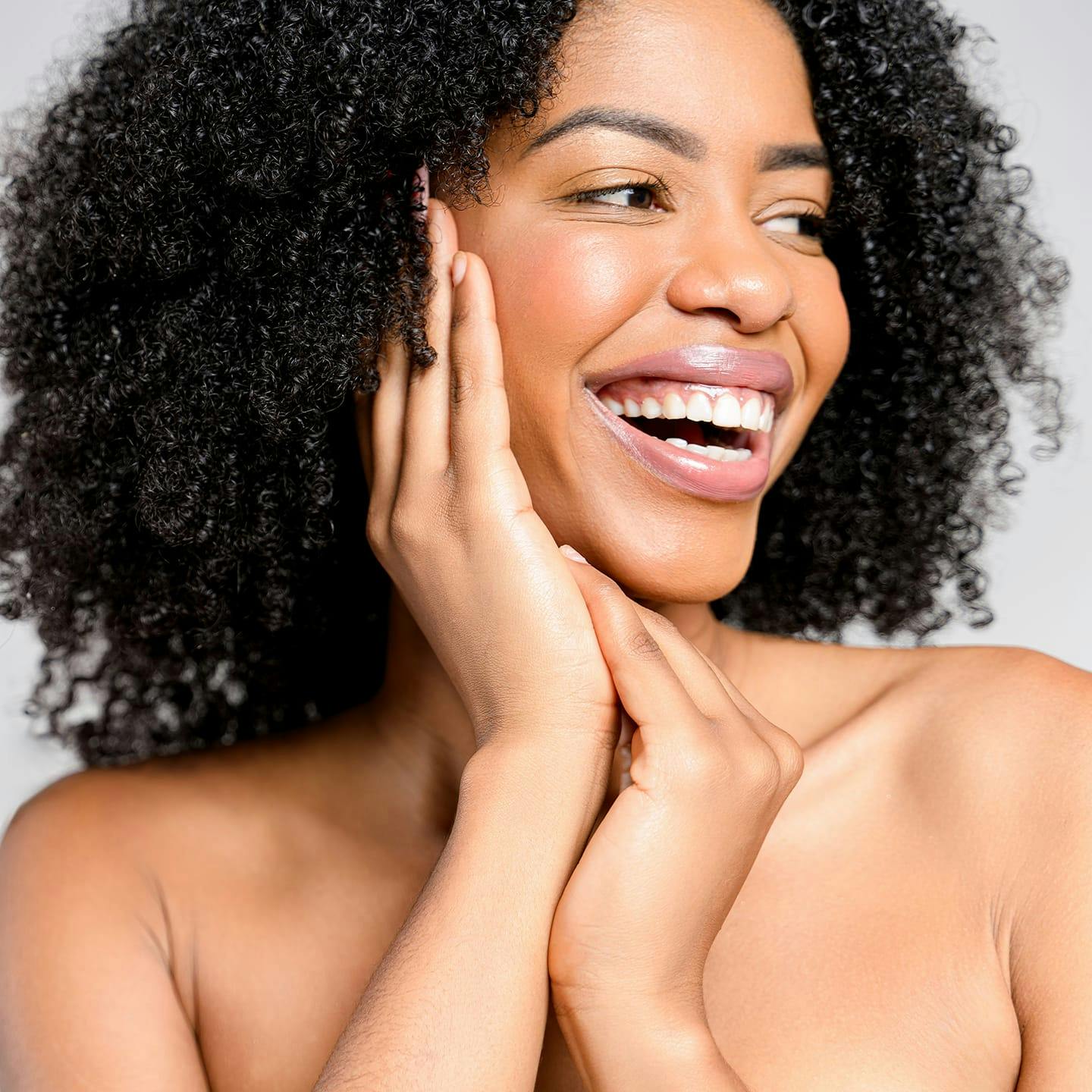 woman with afro smiling to the right with hand touching the side of her face