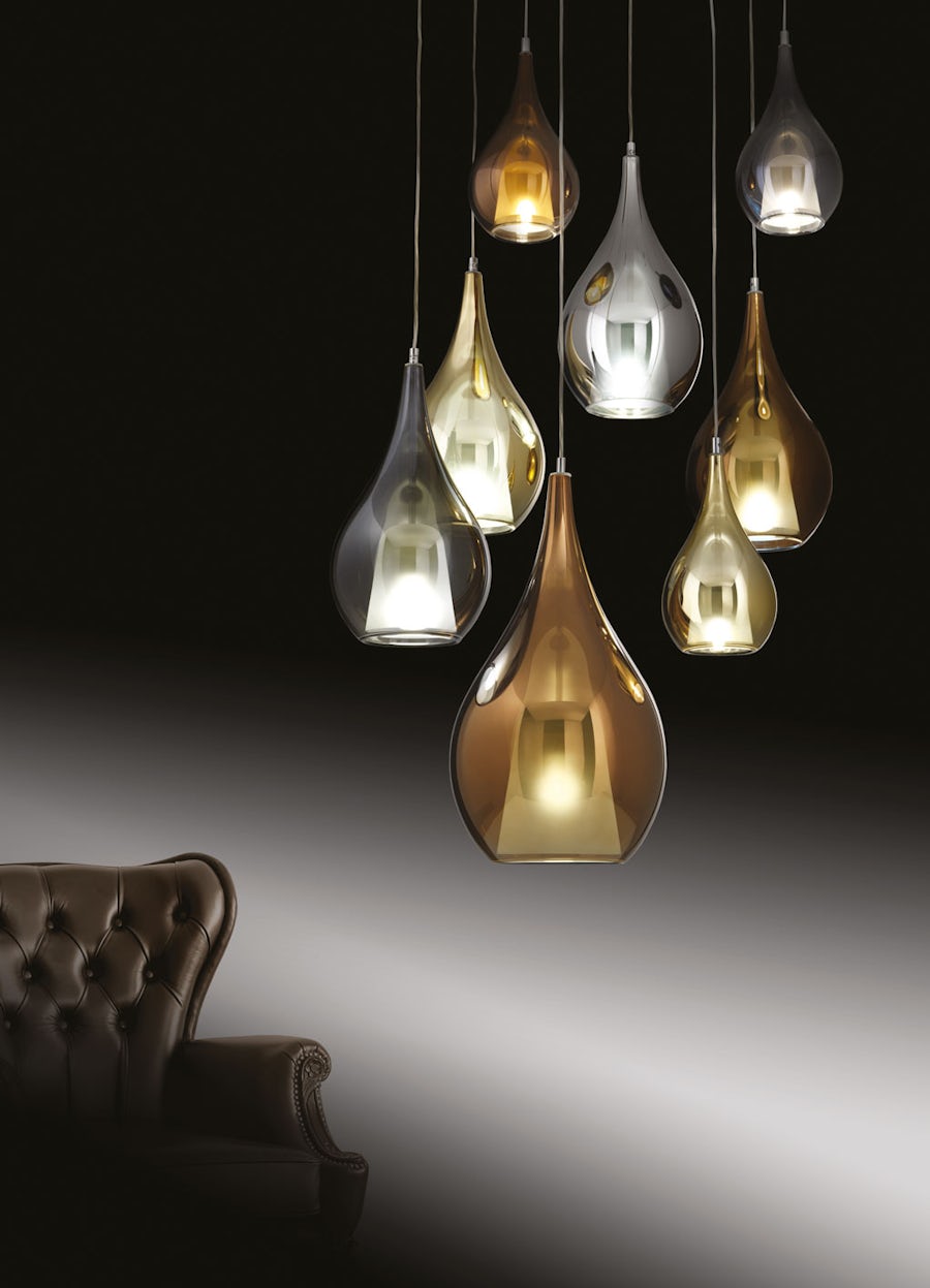 Pendelleuchten aus Metall und Glas hängen über einem getufteten braunen Ledersessel vor einem dunklen Hintergrund.