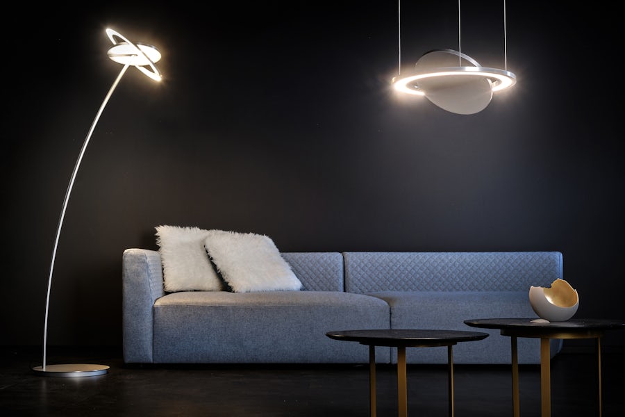 Modernes Wohnzimmer mit graüm Sofa, zwei runden schwarzen Tischen, Stehlampe und runder Deckenleuchte vor einer dunklen Wand.