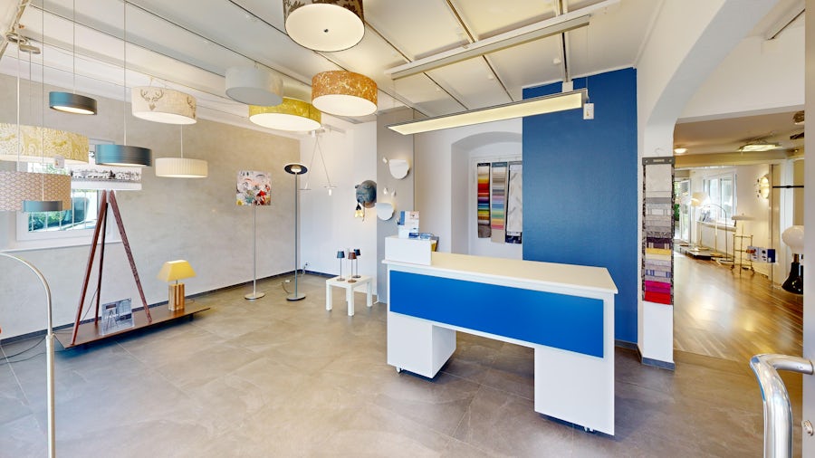 Beleuchtungsausstellungsraum mit Decken- und Stehlampen, blaüm Empfangspult, Ausstellungsmustern und hellem Holzfussboden.