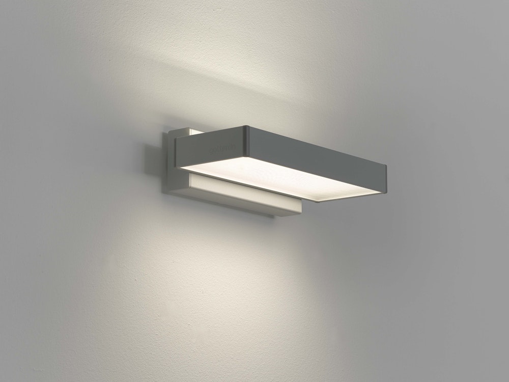 Eine rechteckige moderne Wandleuchte streut das Licht auf einer schlichten hellgraün Wand sanft nach oben und unten.