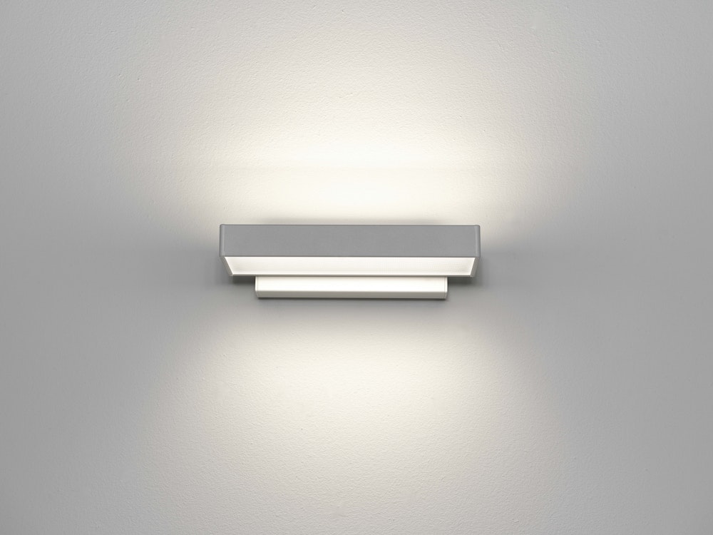 Eine rechteckige moderne Wandleuchte wirft ihr Licht nach oben und unten und beleuchtet sanft eine schlichte weisse Wand.