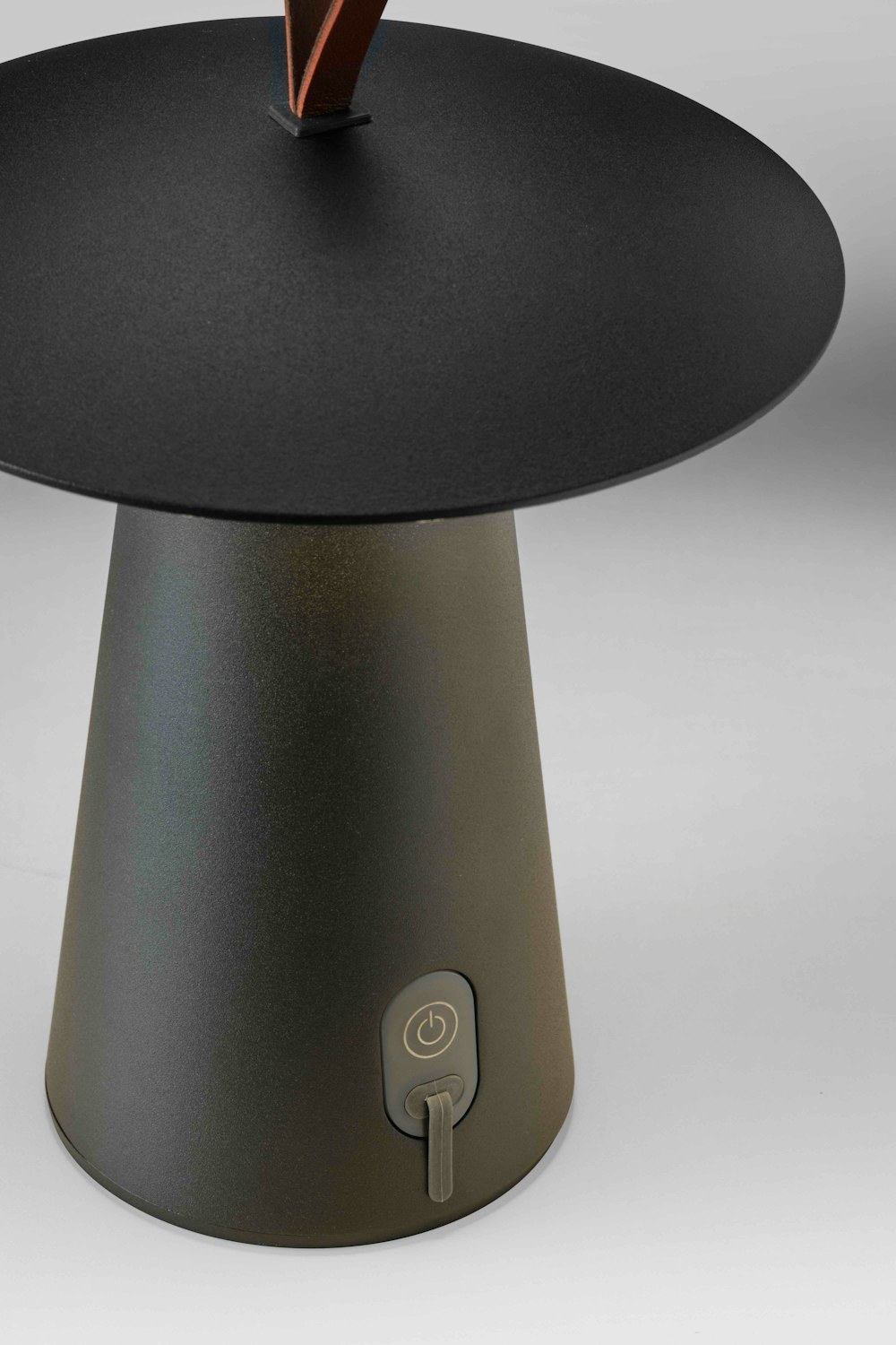 Nahaufnahme einer modernen, kegelförmigen Lampe mit rundem Schirm, mit Einschaltknopf und Schalter am Sockel, vor einem schlichten Hintergrund.