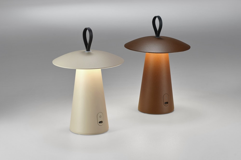 Zwei moderne pilzförmige Tischlampen mit konischen Sockeln und Schlaufengriffen, eine beige und eine braun, beleuchtet auf einer graün Oberfläche.