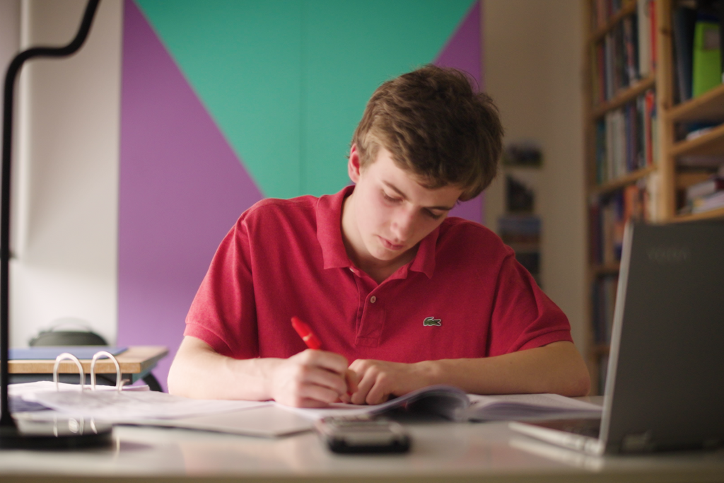 Simon werkt hard achter zijn laptop en maakt notities op papier