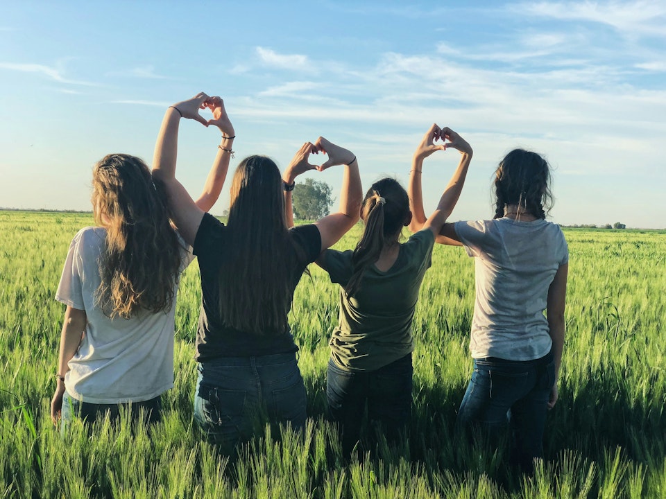 Vier meiden op een rij in het gras, die hartjes maken met hun handen